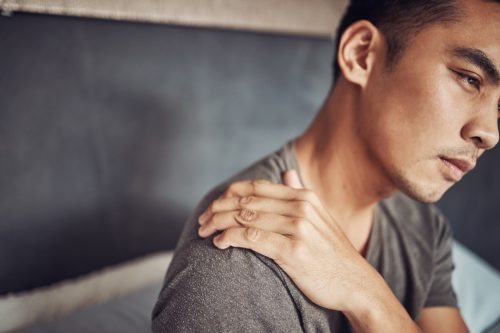 Shot of a young man experiencing shoulder pain after waking up in bed at home