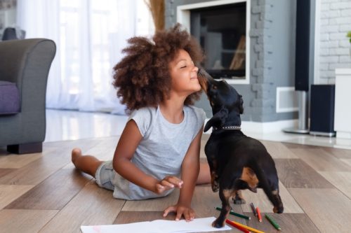 little girl touching her nose to her dog's nose while on the floor