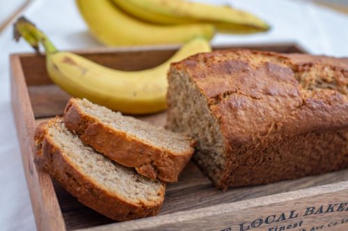banana bread cut into slices with bananas in the background