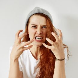 woman with red hair and a gray beanie angry with her hands out