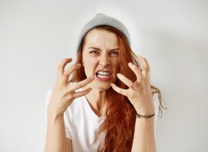woman with red hair and a gray beanie angry with her hands out