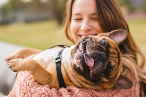Tânără zâmbind în timp ce ține un câine mic afară