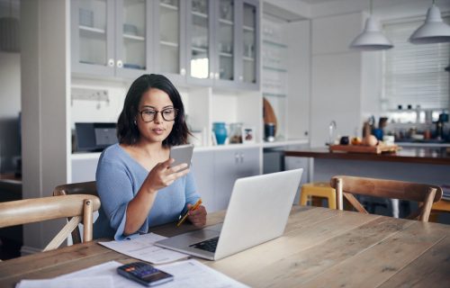 Photo of young woman using mobile phone and laptop while working from home