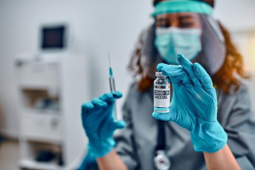 Vaccination and preservation and protection of health. A female doctor in a protective mask and protective medical gloves holds a covid-19 vaccine and a syringe.