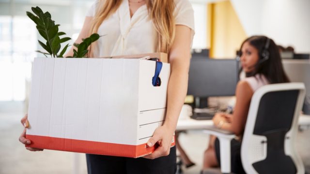 Fired female employee holding box of belongings in an office