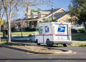 USPS vehicle driving through a residential neighborhood on a sunny day