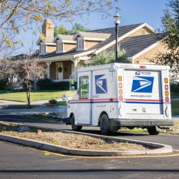 USPS vehicle driving through a residential neighborhood on a sunny day