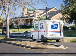 USPS vehicle driving through a residential neighborhood on a sunny day