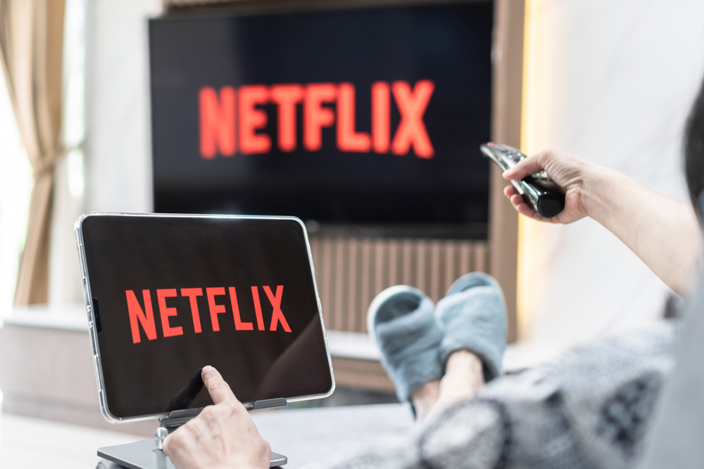 A person sitting on a couch watching Netflix on their TV and tablet