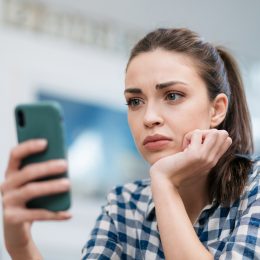 A young woman looking at a message on her phone with a concerned look on her face.