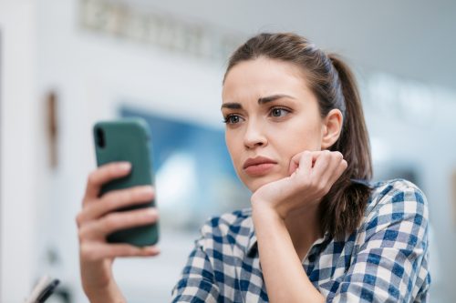 Млада жена гледа съобщение на телефона си със загрижено изражение.