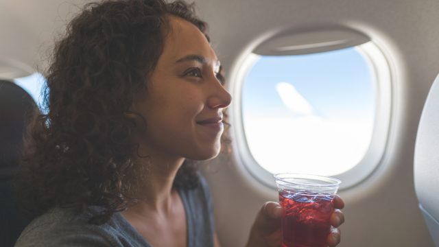 A woman drinking a beverage or cocktail on a flight