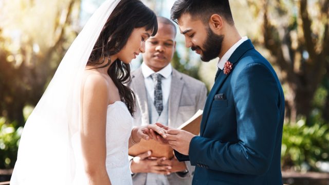 Cropped shot of an affectionate young groom slipping a ring on to his bride's finger while standing at the altar on their wedding day