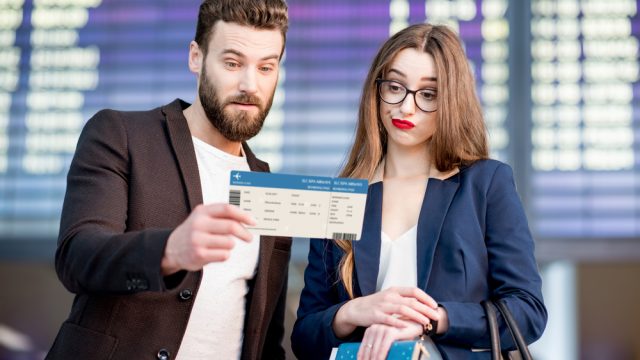 A couple looking at their flight boarding pass with a concerned look on their faces