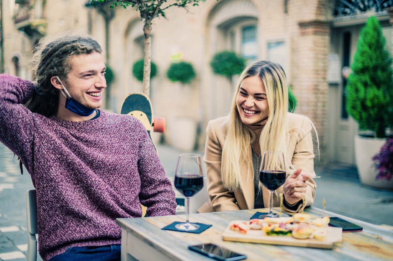A young couple drinking wine on a date with their face masks pulled down