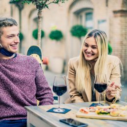 A young couple drinking wine on a date with their face masks pulled down