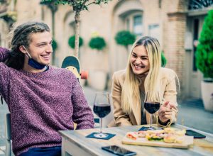 A young couple drinking wine on a date with their face masks pulled down