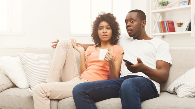 A young man and woman watching TV with a confused or disappointed look on their faces