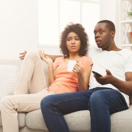 A young man and woman watching TV with a confused or disappointed look on their faces