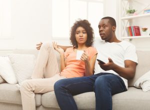 A young man and woman watching TV with a confused or disappointed look on their faces