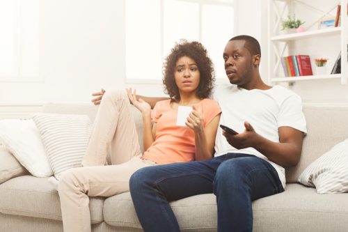 A young man and woman watching TV with a confused or disappointed look on their faces