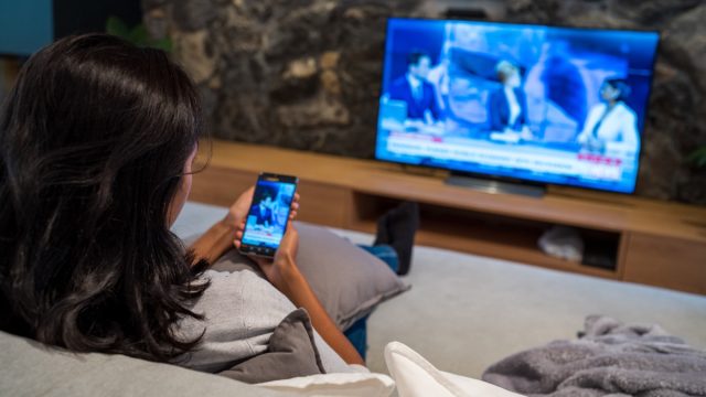 Young woman watching news on television and smart phone