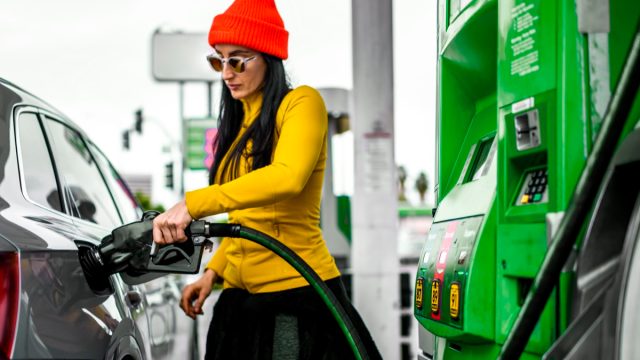 A fancy woman pouring some fuel in her car.