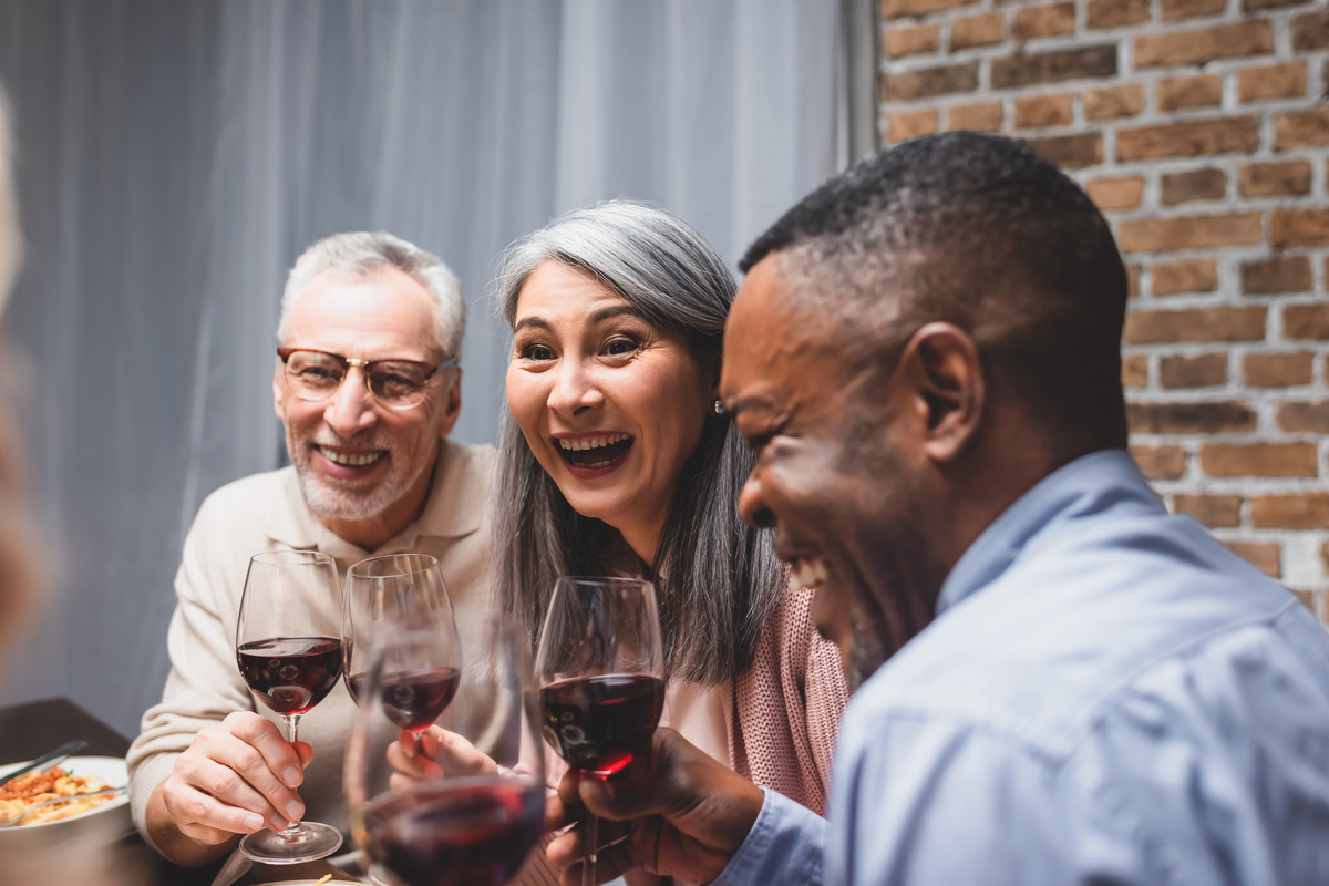 Drei Freunde genießen zusammen Wein: ein älterer Weißer, eine Asiatin und ein Schwarzer mittleren Alters