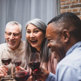 three friends enjoying wine together: an older white man, an Asian woman, and a middle aged Black man