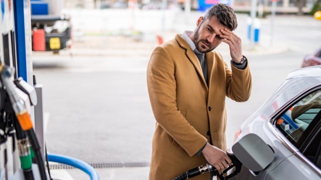 Worried man refueling his car's tank at the gas station in the city.