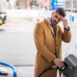 Worried man refueling his car's tank at the gas station in the city.