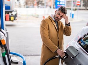 Worried man refueling his car's tank at the gas station in the city.