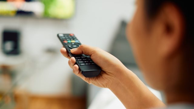 Close-up of woman watching Tv and changing channels with remote controller at home.