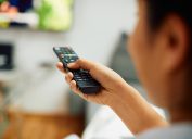 Close-up of woman watching Tv and changing channels with remote controller at home.