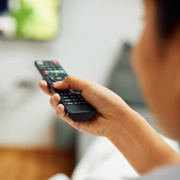 Close-up of woman watching Tv and changing channels with remote controller at home.