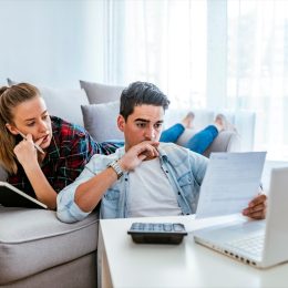 Photo of Depressed young couple doing their accounting in their living room during the day. Young couple calculating their domestic bills at home. Family budget and finances. Young woman doing accounts together with her husband at home, planning new purchase. Serious female making necessary calculations.