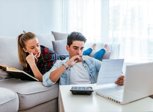 Photo of Depressed young couple doing their accounting in their living room during the day. Young couple calculating their domestic bills at home. Family budget and finances. Young woman doing accounts together with her husband at home, planning new purchase. Serious female making necessary calculations.