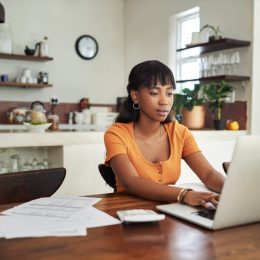 Shot of a young woman sitting with her laptop and paperwork at home