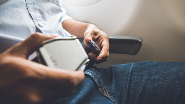 A man buckling his seatbelt on a plane
