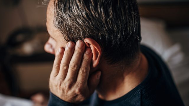 A middle-aged man touching his ear maybe suffering from hearing loss