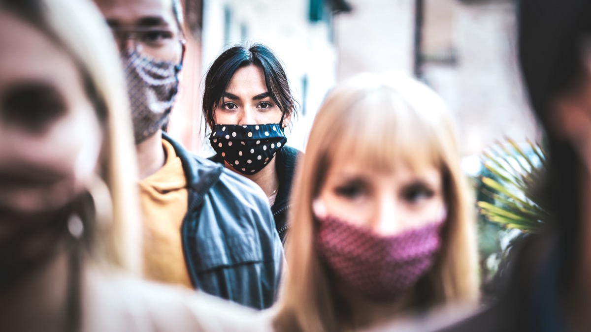 Menschenmenge, die sich auf den mit Gesichtsmasken bedeckten Straßen der Stadt bewegt - Neues normales menschliches Zustands- und Gesellschaftskonzept - Fokus auf durchschnittliche Frau mit schwarzer Gesichtsmaske - entsättigter Kontrastfilter