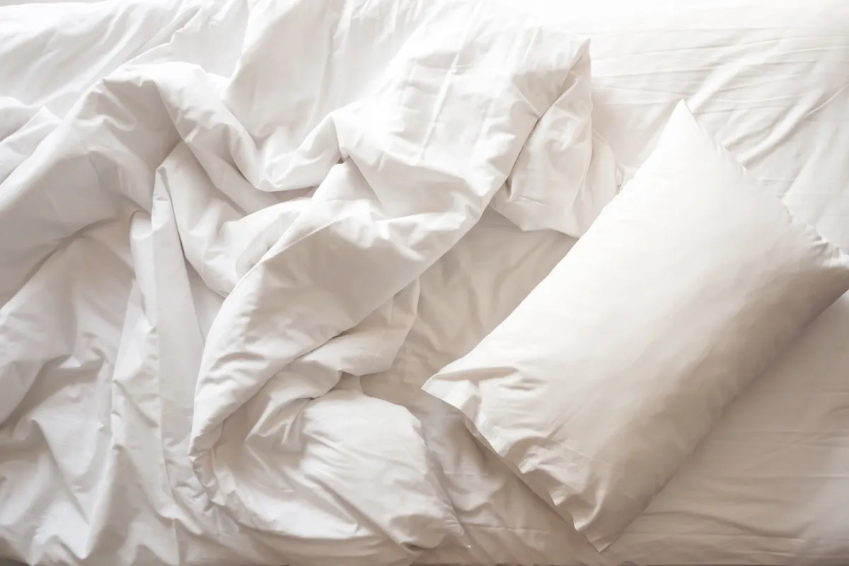 Giường bừa bộn.  Một chiếc gối trắng với chăn trên chiếc giường còn dang dở.  Khái niệm thư giãn sau buổi sáng.  Với ánh sáng cửa sổ.  Nhìn từ trên xuống.