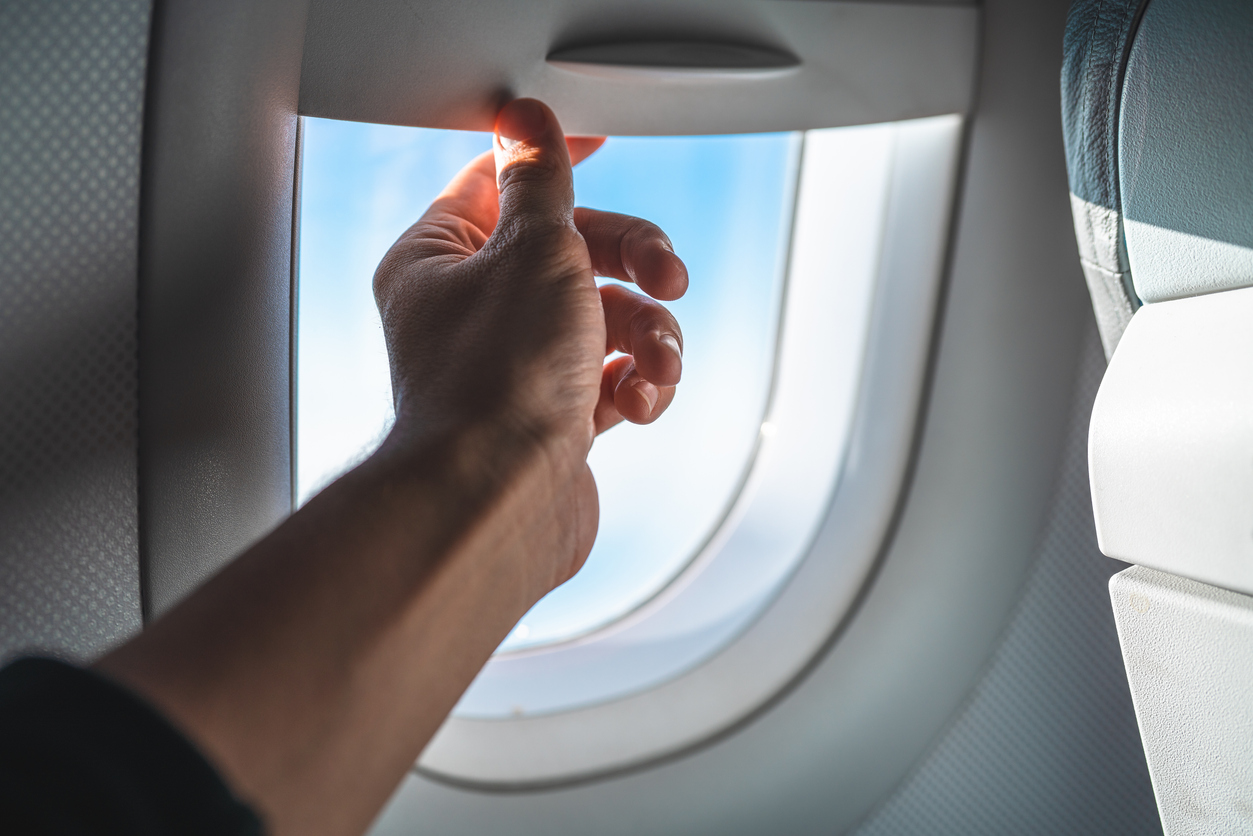 A hand pulling down a plane window shade or blind