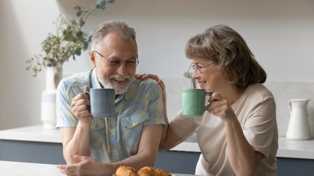 A senior couple sitting in the kitchen while drinking coffee and eating breakfast