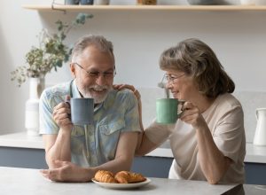 A senior couple sitting in the kitchen while drinking coffee and eating breakfast