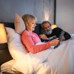A senior couple lying in bed while using a tablet and reading before going to sleep