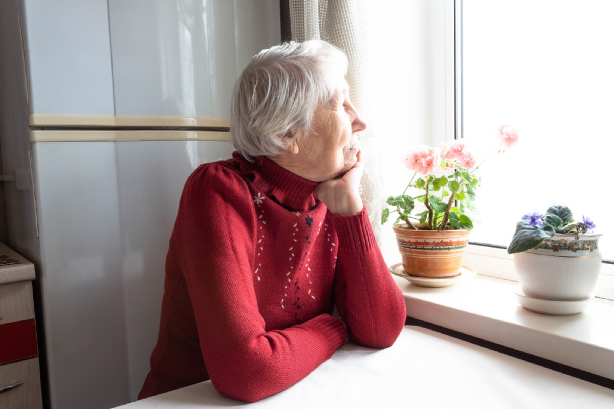 lonely older woman staring out the window next to flowers
