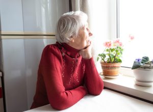 lonely older woman staring out the window next to flowers