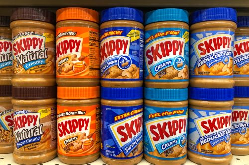 Grocery store shelf with jars of Skippy brand peanut butter in various flavors