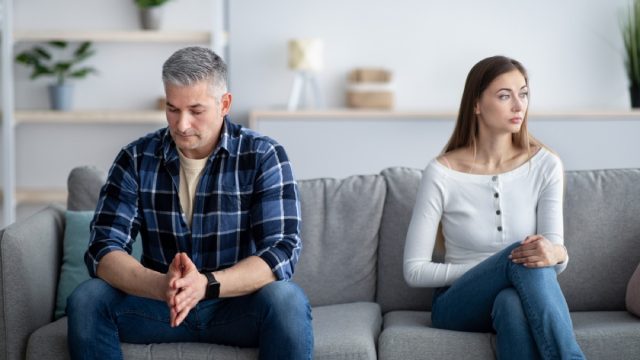 man and woman sitting on opposite ends of the couch, not looking at each other